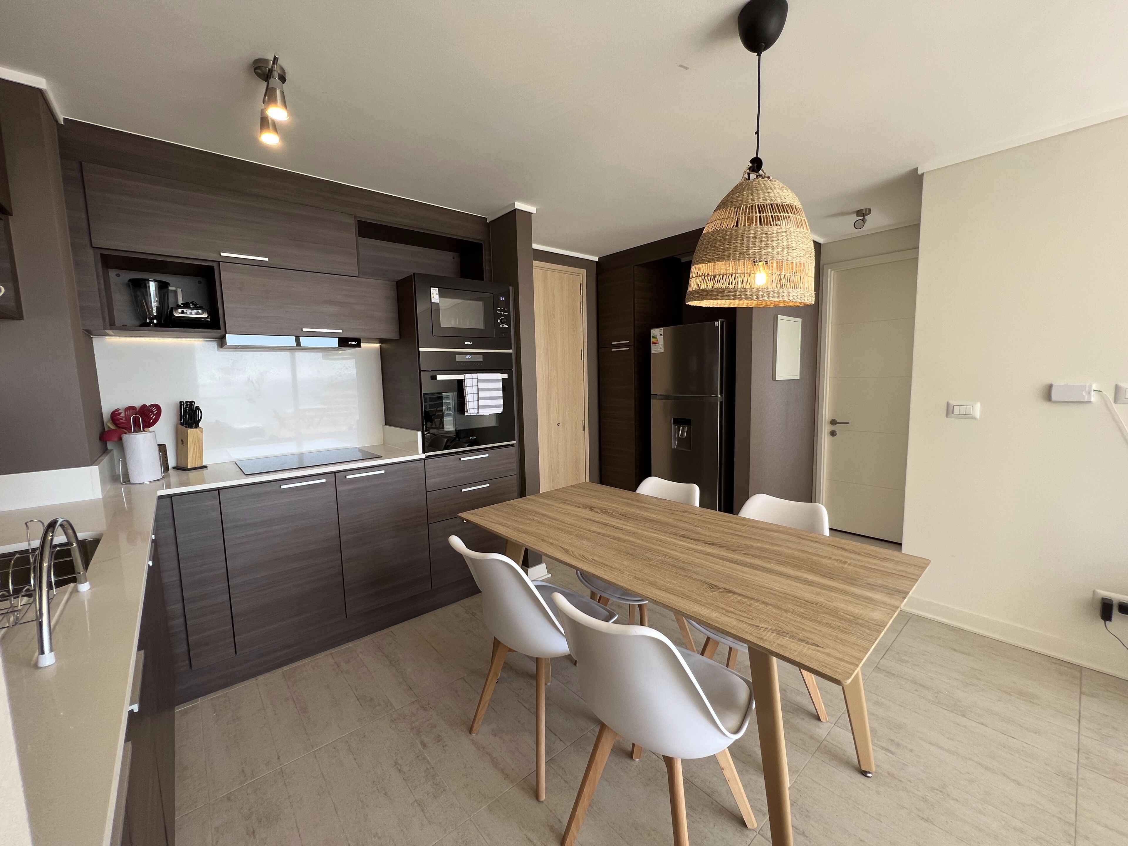 Eine moderne Küche mit dunklen Schränken, einem Holztisch und weißen Stühlen.