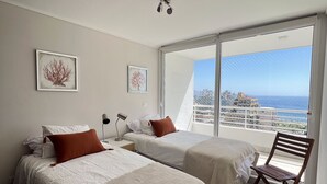 A bedroom with two beds, a chair, and a large window with a city view. - Vina del Mar 2BR sea views & balcony (Viña del Mar)