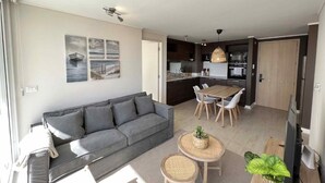 A modern living room with a sofa, dining table, and chairs, a kitchen area, and artwork on the walls. - Vina del Mar 2BR sea views & balcony (Viña del Mar)