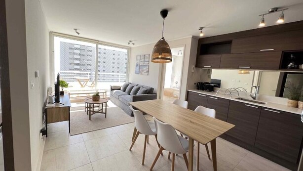 A modern kitchen with a dining area, large windows, and a view of a building outside. - Vina del Mar 2BR sea views & balcony (Viña del Mar)