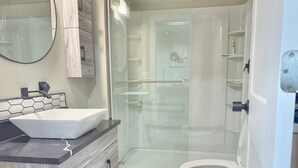 Ein Badezimmer mit einem Aufsatzwaschbecken, einem Holz-Waschtisch, einer Glasdusche und einer Toilette.