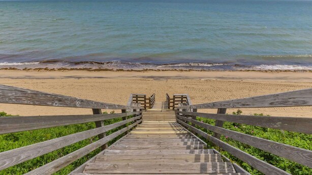A wooden staircase leading to a beach with a view of the ocean. - Hydrangea Lane Beach Cottage (Mashpee)