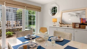 A dining area with a table set for two, a ceiling fan, and a window with a view of greenery. - Hydrangea Lane Beach Cottage (Mashpee)