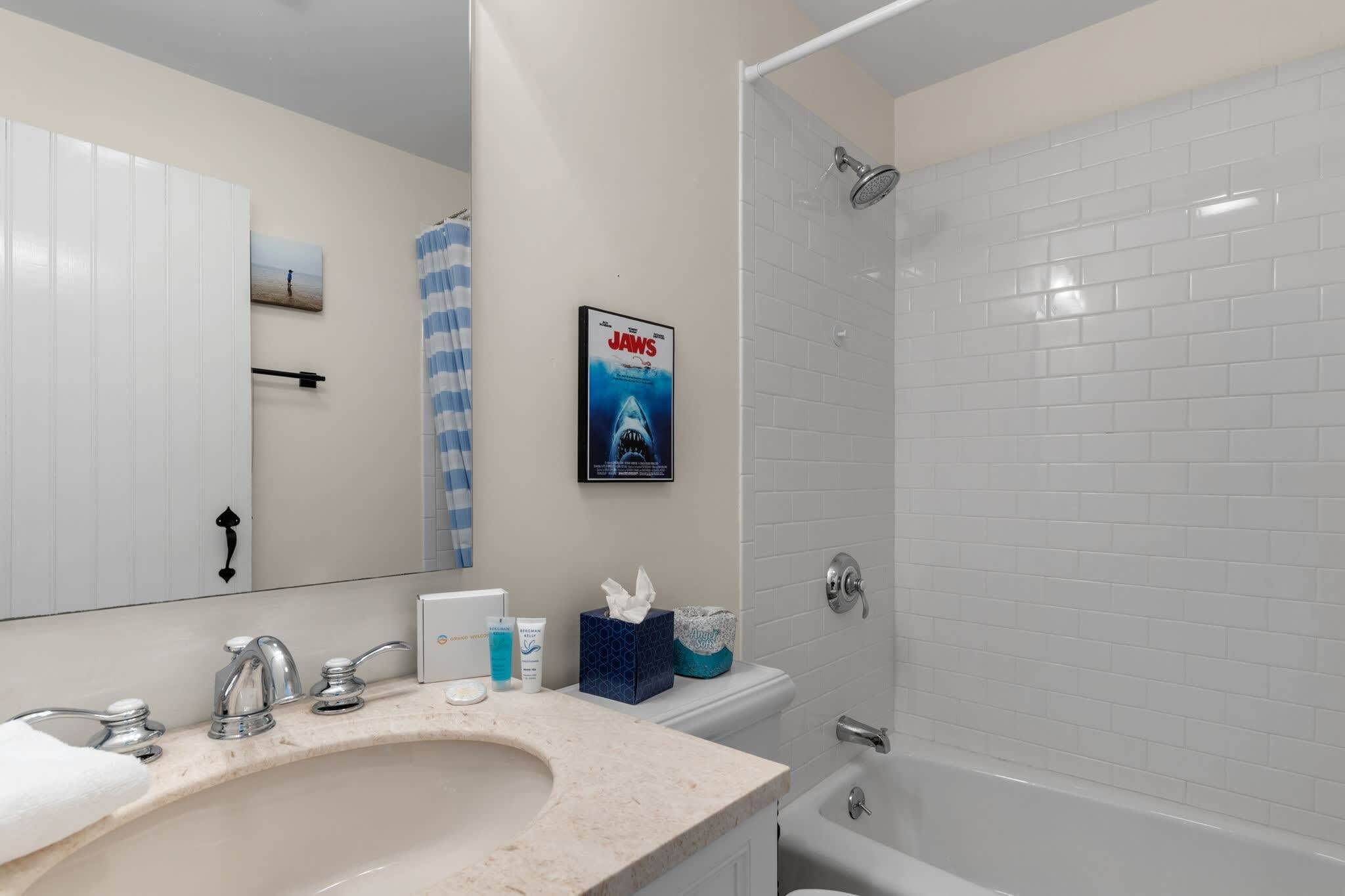 A bathroom with a sink, mirror, shower, and a poster on the wall.
