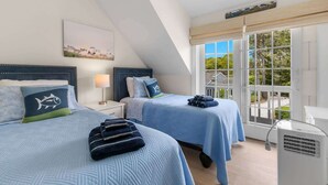 A bedroom with two beds, a window with a view, and a bedside table with a lamp. - Hydrangea Lane Beach Cottage (Mashpee)