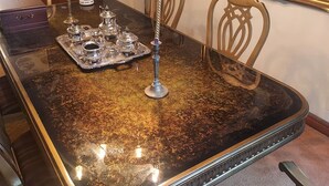 Una mesa de comedor con superficie reflectante, rodeada de sillas y una lámpara de araña.