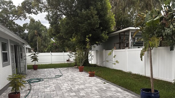 Une terrasse dallée agrémentée de plantes en pot, une clôture blanche et un bâtiment doté d’une fenêtre.