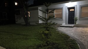 Vue nocturne d’un bâtiment avec une pelouse bien entretenue, un petit arbre et une zone d’entrée pavée.