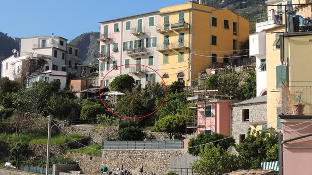 Un pueblo costero con edificios de varios pisos, muros de piedra y un cerro al fondo.