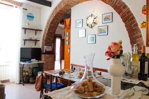 A dining area with a brick archway, a table set for two, and various decorative items including a clock and framed pictures on the wall. - Apartment with a private garden and ocean view, near hiking trails (Corniglia)