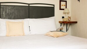 Una cama con cabecera, almohadas, una mesita de noche con lámpara y un cuadro en la pared.