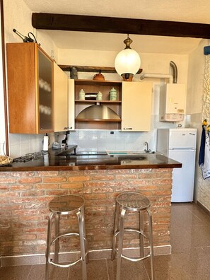 A kitchen with a brick island, wooden cabinets, a stainless steel range hood, and a hanging light fixture. - Apartment with a private garden and ocean view, near hiking trails (Corniglia)