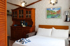 A bedroom with a wooden headboard, a bed with white linens, a wooden dresser with glass doors, and a painting of a coastal scene on the wall. - Apartment with a private garden and ocean view, near hiking trails (Corniglia)