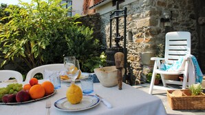 Un espacio de comedor al aire libre con una mesa preparada para dos personas, que incluye una bandeja de frutas, un vaso de agua y un bol de pan.