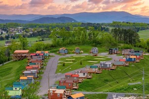 A rural village with small houses arranged around a central road, surrounded by green fields and mountains in the background.