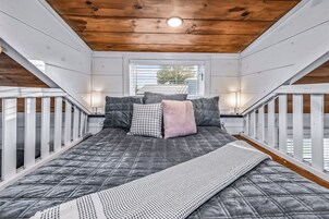 A loft bedroom with a bed, pillows, a blanket, and a view of the outside.