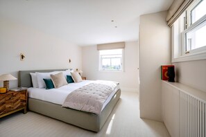 Ein Schlafzimmer mit Bett, Nachttisch, Lampe, Fenster, Heizkörper und einem an der Wand montierten Lautsprecher.