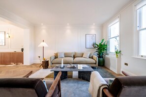 Ein modernes Wohnzimmer mit einer Couch, einem Couchtisch und Sesseln. Ein Heizkörper, eine Lampe und eine Pflanze sind ebenfalls vorhanden.