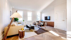 Ein modernes Wohnzimmer mit Sofa, Couchtisch und Lampe, ein Essbereich mit Stühlen und eine Küche mit Fernseher.