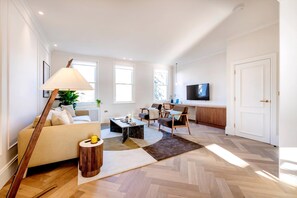 Ein modernes Wohnzimmer mit Sofa, Couchtisch und Lampe, ein Essbereich mit Stühlen und eine Küche mit Fernseher.