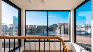 Ein Balkon mit großen Fenstern, einem Hollerker und Blick auf Gebäude und einen klaren Himmel.