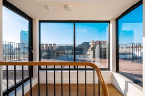 Ein Balkon mit großen Fenstern, einem Hollerker und Blick auf Gebäude und einen klaren Himmel.