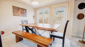 Een eetruimte met een houten tafel en banken, een plafondlamp, een brandblusser en een deur met uitzicht naar buiten.