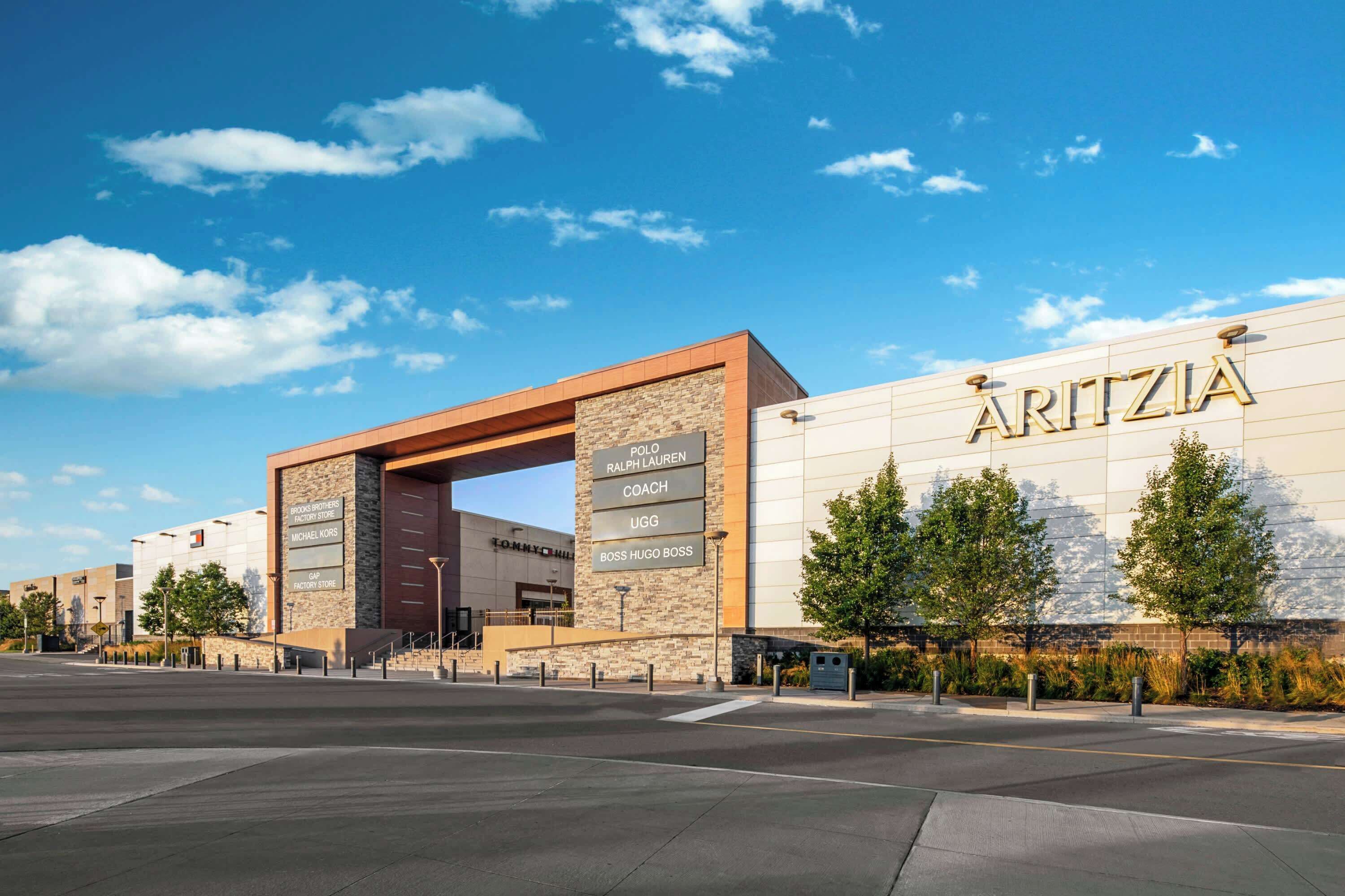 A modern building with a prominent sign reading 'ARITZIA' and a sign for 'Polo Ralph Lauren Coach UGG Boss Hugo Boss.'