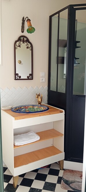 Un baño con un tocador blanco, un espejo, una lámpara verde montada en la pared y un suelo a cuadros.