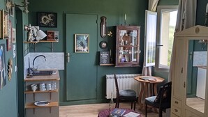 Una habitación con pared verde, un armario de madera, un radiador, una mesita y una silla.
