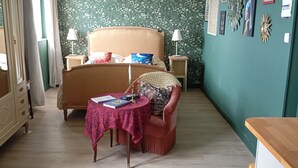 Un dormitorio con cama, mesitas de noche, una silla, una pequeña mesa con libros y un espejo.