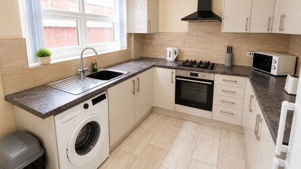 Una cocina compacta equipada con lavadora, microondas, estufa y lavabo.