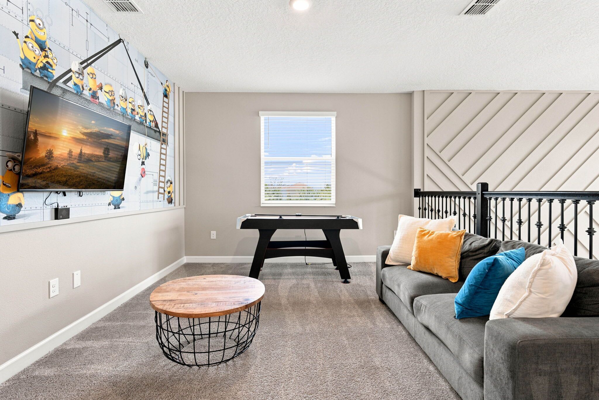 A living room with a pool table, a TV mounted on the wall, and a window with blinds.