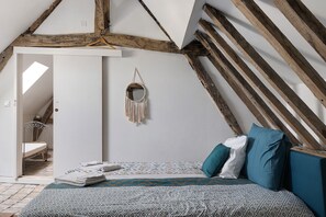 A bedroom with a sloped ceiling, a bed with patterned bedding, and a macramé wall hanging. - Guest Room “Large Space, 2 Bedrooms, Private Bathroom” with Wi-Fi and Air Conditioning (Hommes)