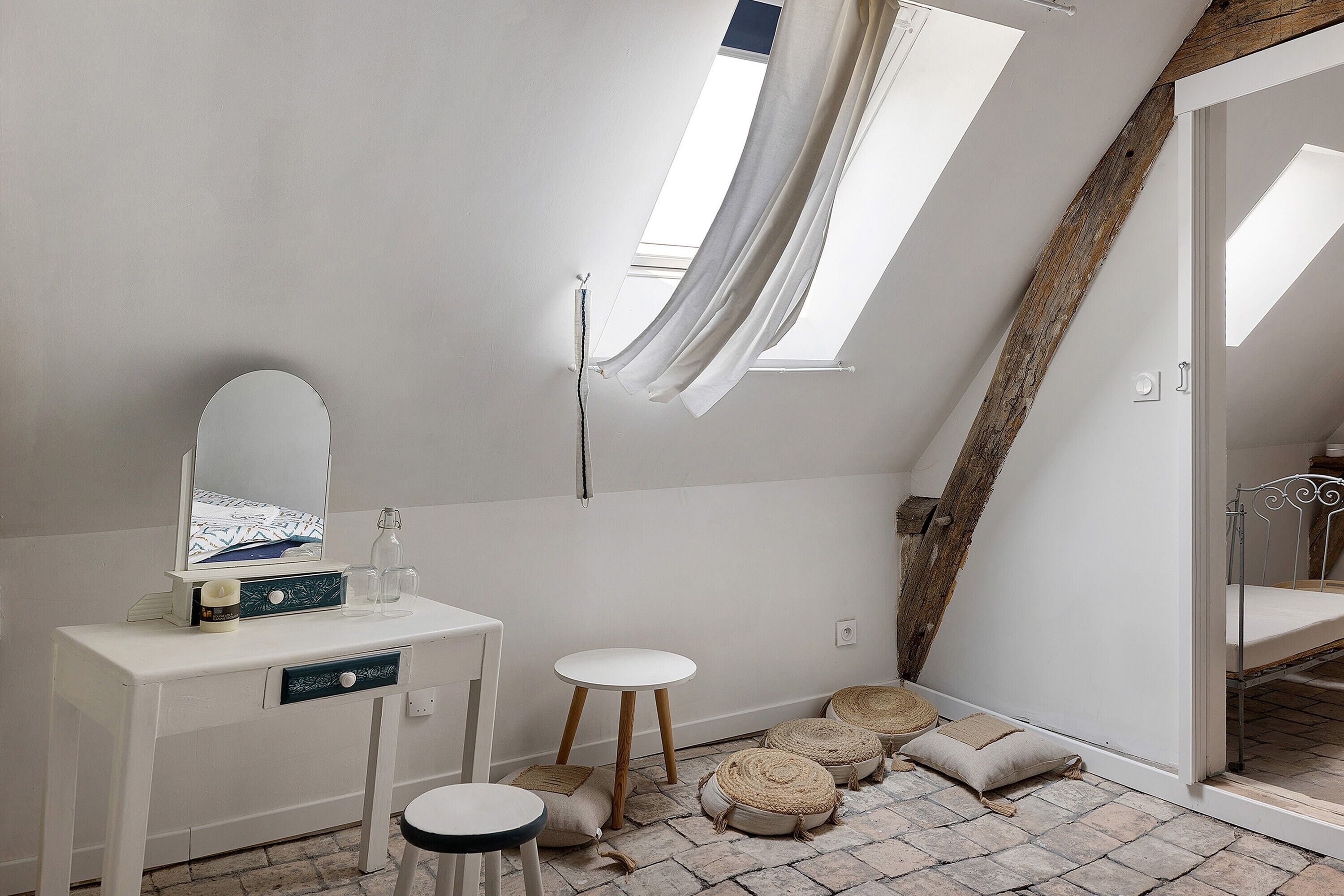 Et soveværelse med et toiletbord, et spejl, en lille skammel og en seng med metalstel. Der er to vinduer, der giver naturligt lys.