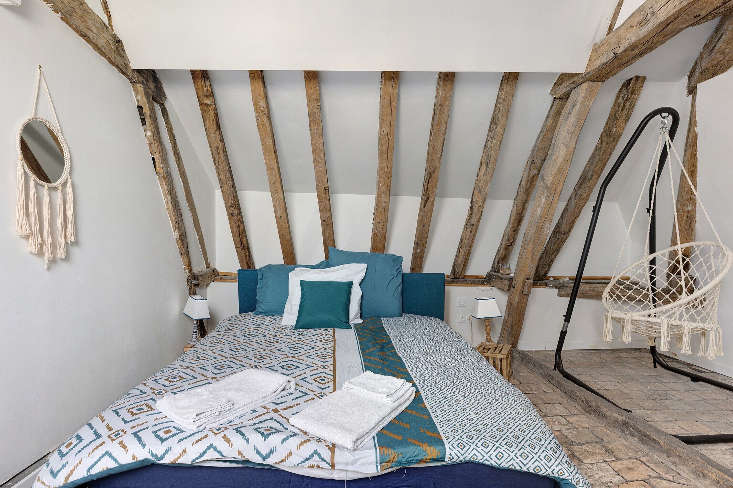 Ein Bett mit gemusterten Betttextilien, ein Wandbehang aus Makramee und ein Hängekorbsessel.