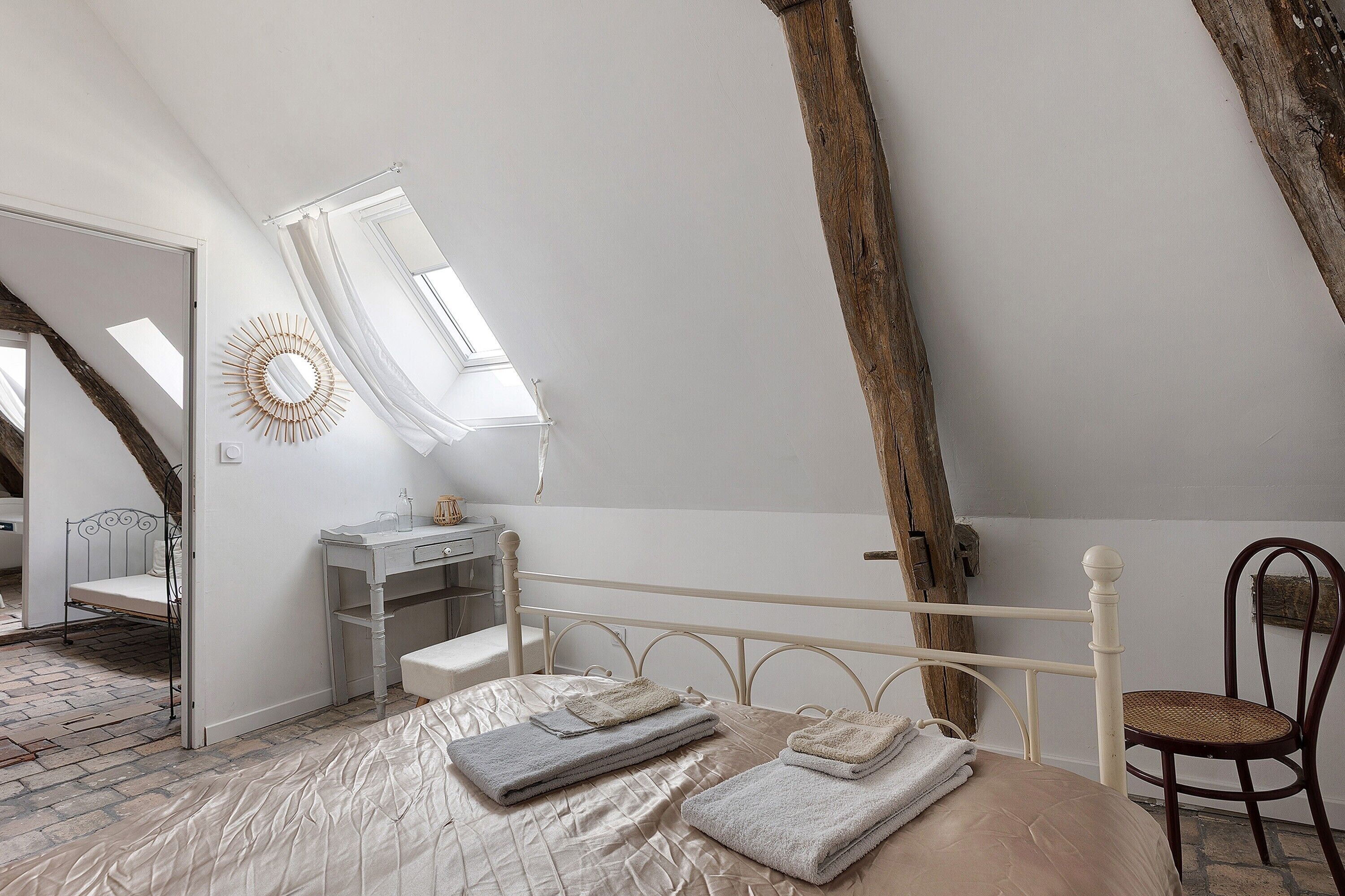 A bedroom with a sloped ceiling, a bed with a headboard, a bedside table, a chair, and a mirror.