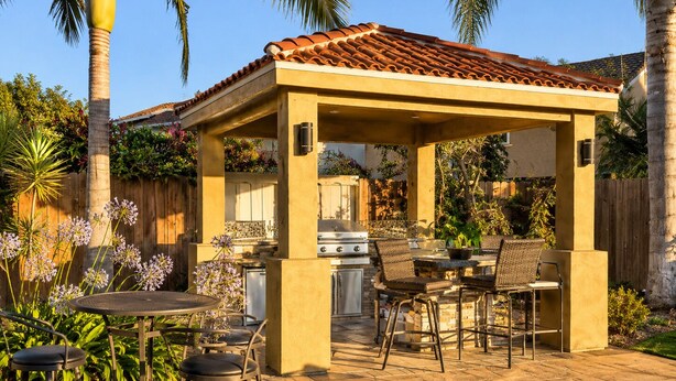Una veranda esterna con zona barbecue coperta, posti a sedere e un piccolo tavolo.