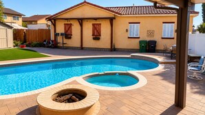 Una piscina con un braciere, un'area patio e una casa con tetto in tegole.