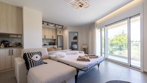 A modern hotel room with a sofa, a bed, a kitchenette, and large windows. - Enclave Luxury Apartments Zante Experience equiped with Jacuzzi,BBQ,GYM (Zakinthos)