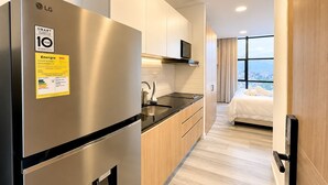 A modern hotel room with a kitchen area, a bed with a city view, and a door with a handle. - King Bed + View Monserrate - 19 floor (Bogotá)