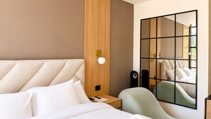 A hotel room with a bed, a seating area, a wall-mounted mirror, and a nightstand with a lamp. - King Bed + View Monserrate - 19 floor (Bogotá)