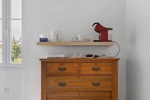 A wooden dresser with drawers, a shelf above holding a tissue box, a kettle, and a red hairdryer.