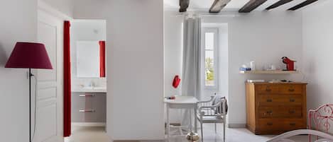 A bedroom with a bed, a dresser, a desk, and a chair. There is a window with curtains, a lamp, and a mirror.