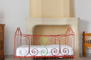 Een bed met metalen frame en een witte matras in een kamer met een beige muur en een open haard.