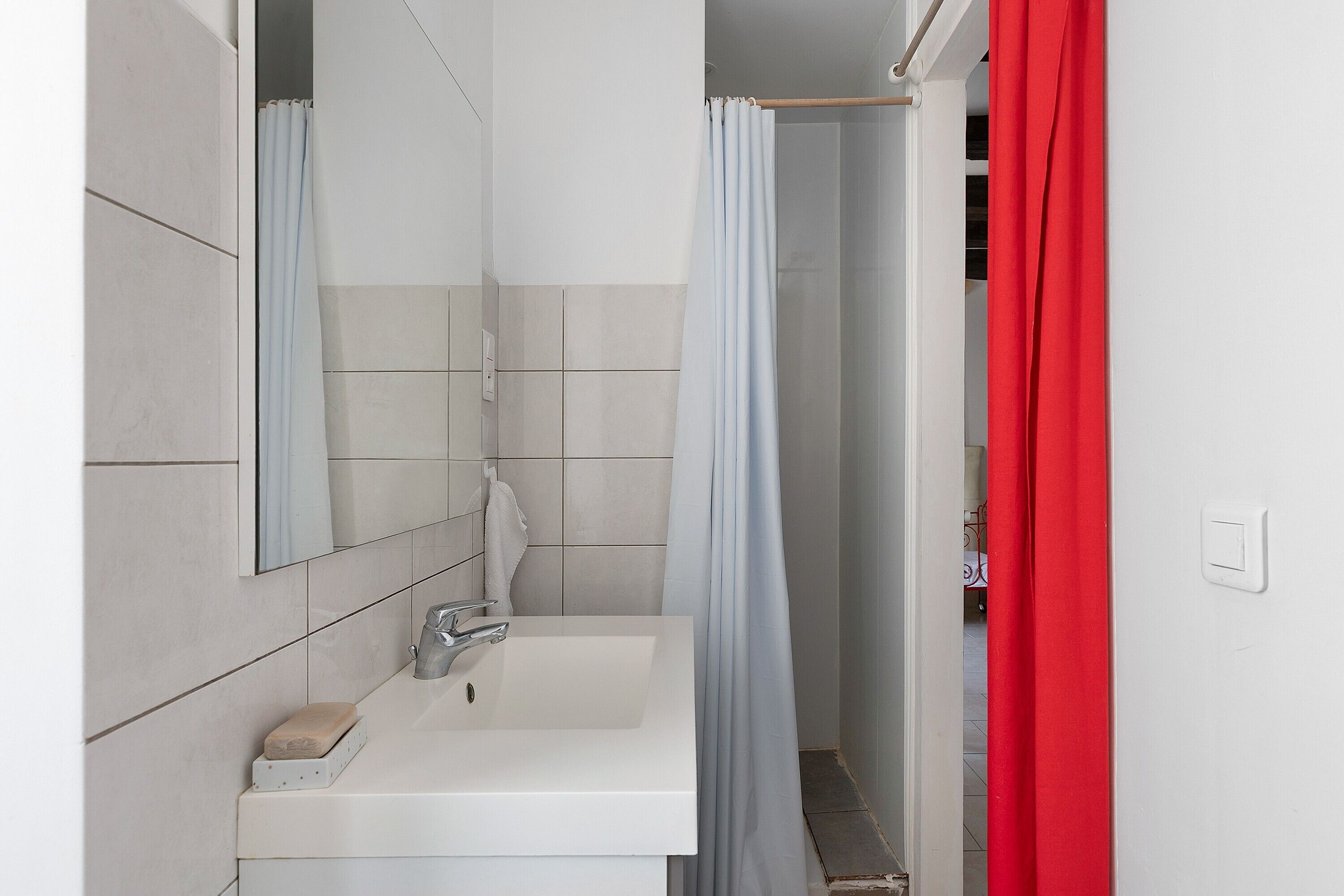 Une salle de bain avec un lavabo blanc, un miroir et un rideau de douche.