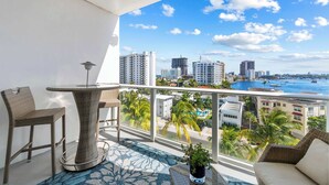 A balcony with wicker furniture, a round table, and a view of the city and water. - Bayside Breeze - Resort Access (Fort Lauderdale)