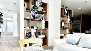 A modern living room with a white sofa, a wooden chair, a round coffee table, and a chessboard. - Bayside Breeze - Resort Access (Fort Lauderdale)