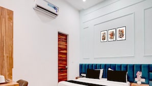 Quarto moderno com escrivaninha de madeira, cama com cabeceira estofada em azul e ar condicionado fixado na parede.