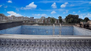 Piscina no terraço com borda em azulejo, escada de metal e vista panorâmica da cidade ao fundo.